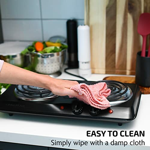 Hand wiping stovetop with a cloth in a kitchen setting.