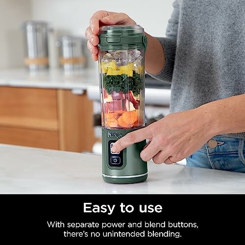 Person using a portable blender with fruits and vegetables inside.